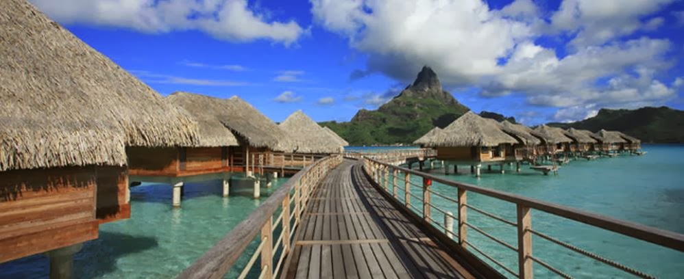 Bora Bora over water with huts and a mountain in the background