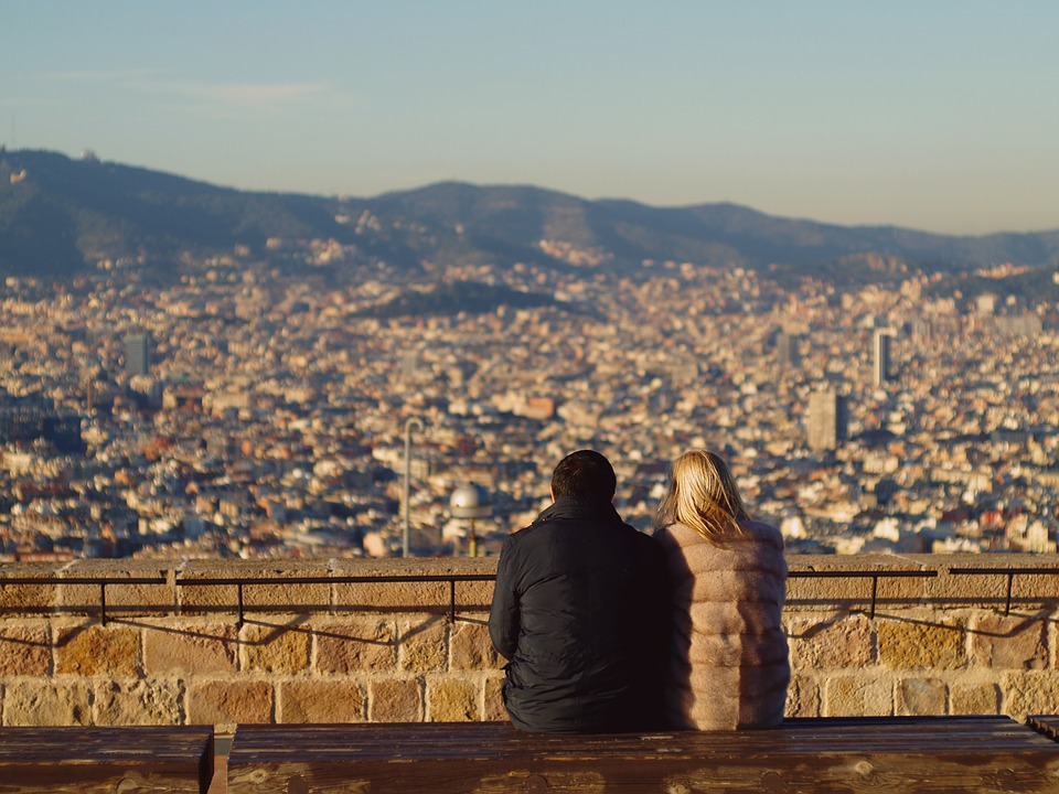 a man and woman sitting on a bench looking at a city