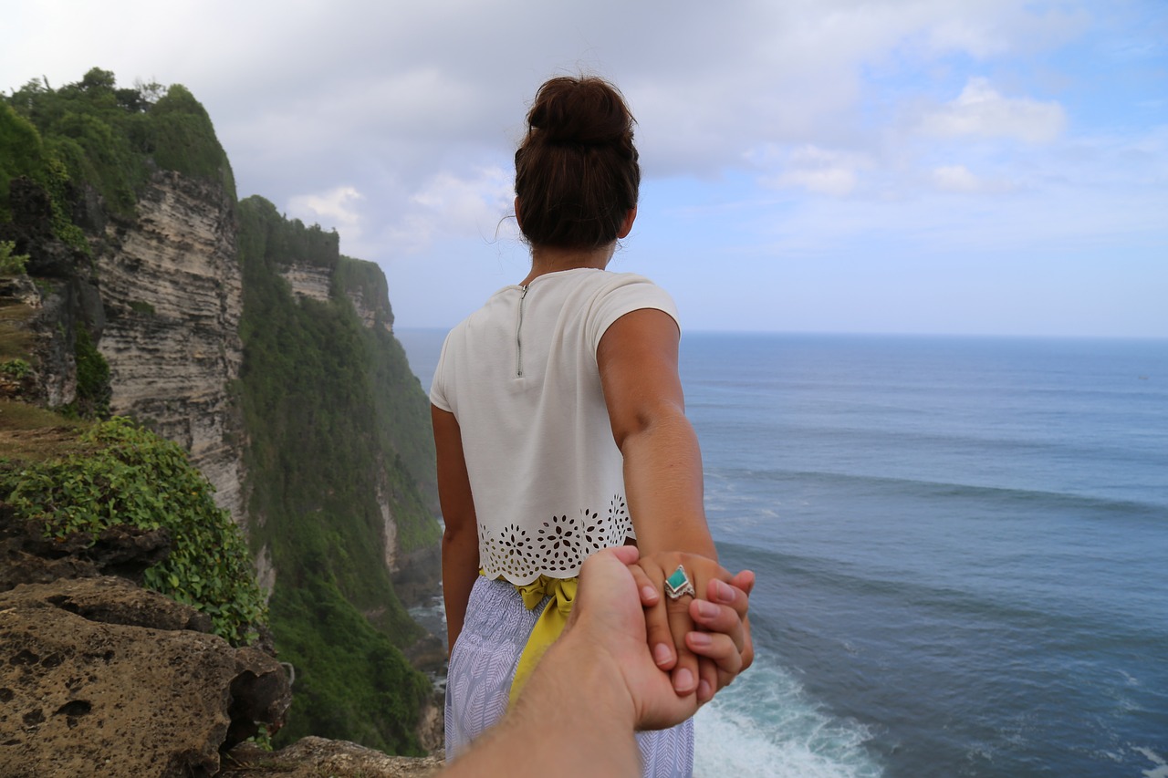 a person holding a hand of a woman on a cliff overlooking the ocean