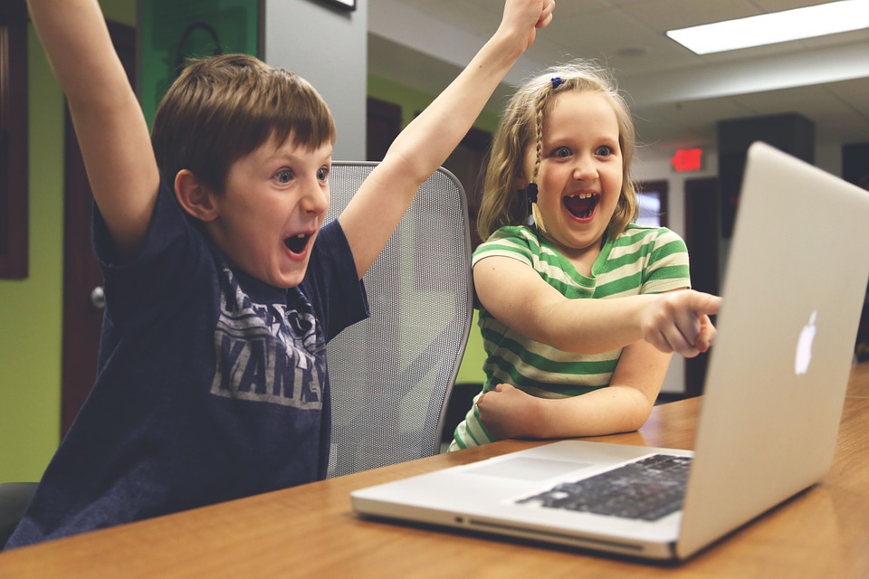 a boy and girl with their hands up in front of a laptop