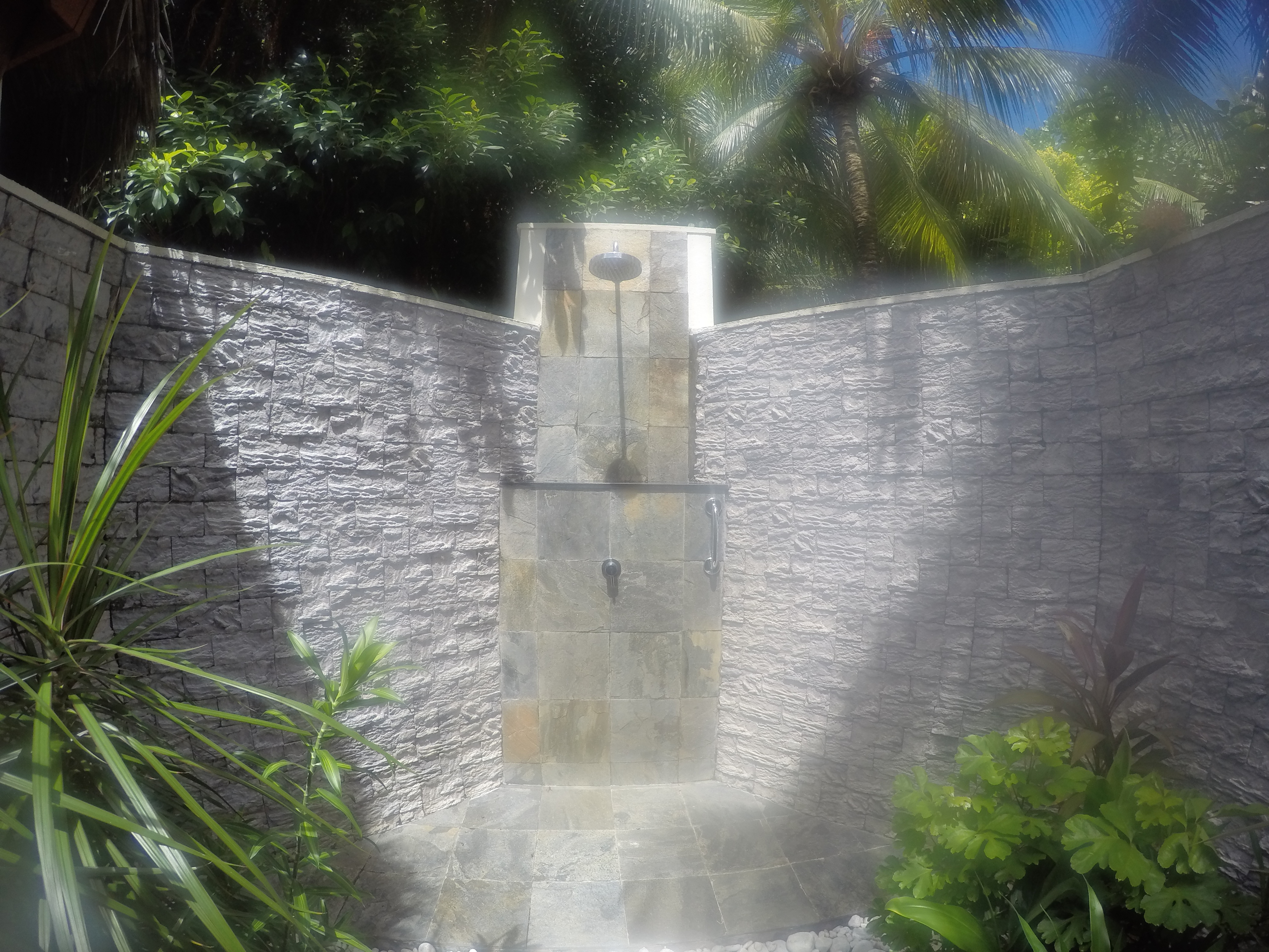 a outdoor shower with a stone wall and plants