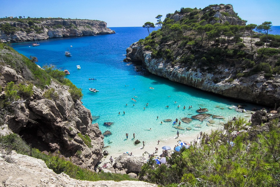 a beach with many people and boats in the water with Calanques National Park in the background
