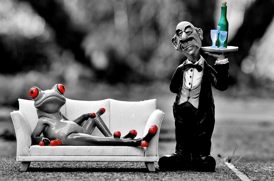 a statue of a man holding a tray of champagne and a frog lying on a couch