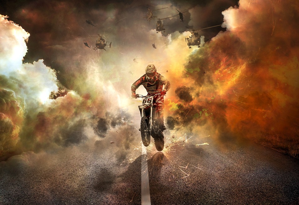 a man riding a motorcycle on a road with smoke and fire