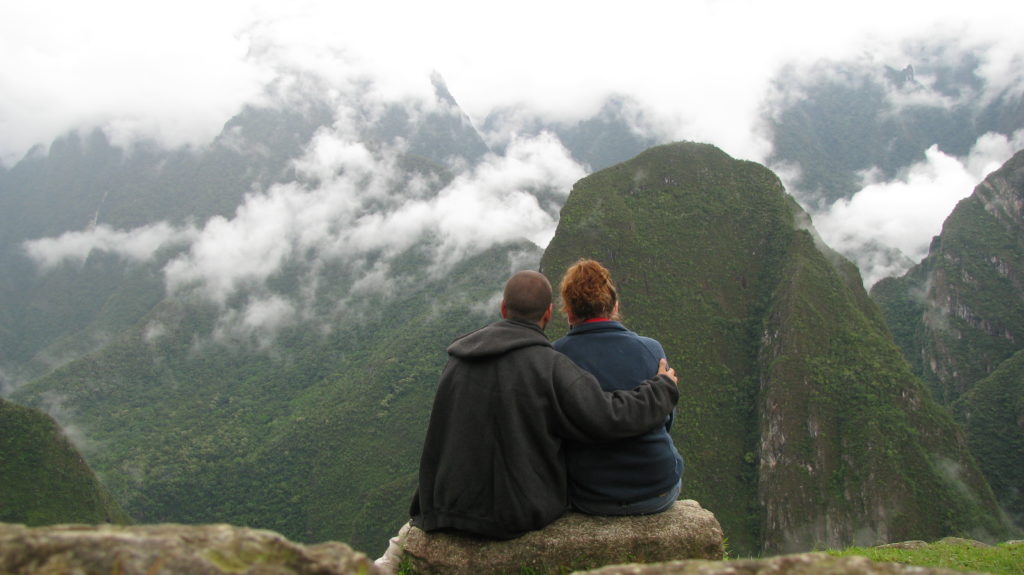 a man and woman sitting on a rock looking at the mountains