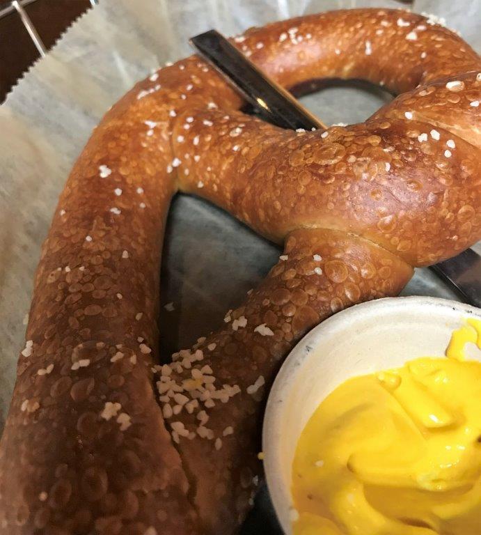 a pretzel with a spoon next to a bowl of cheese