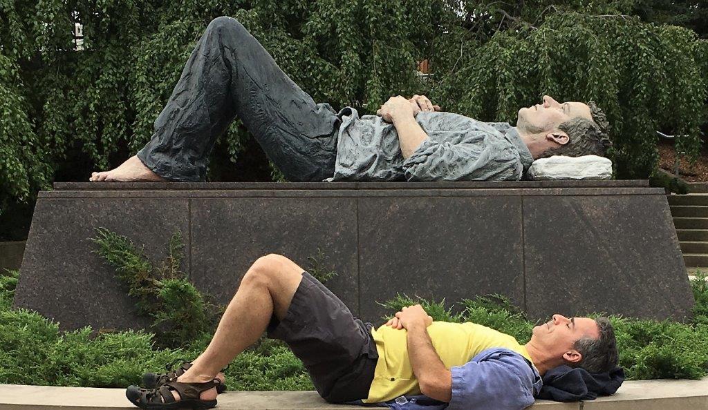 a man lying on a bench next to a statue of a man