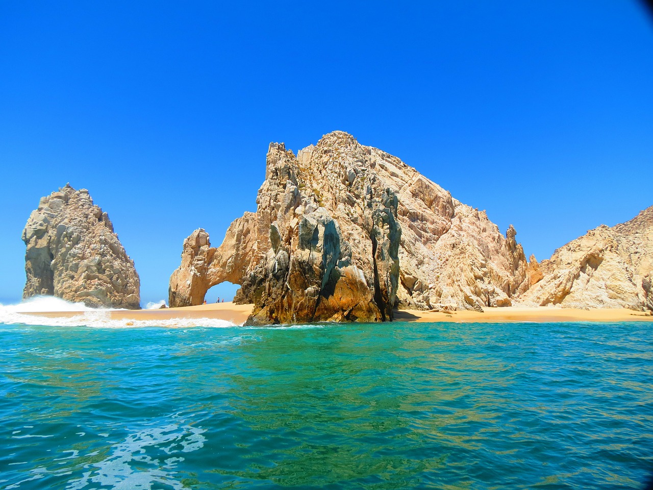 a large rock formation on a beach with Arch of Cabo San Lucas in the background