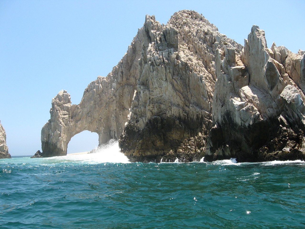 a large rock formation in the ocean with Arch of Cabo San Lucas in the background