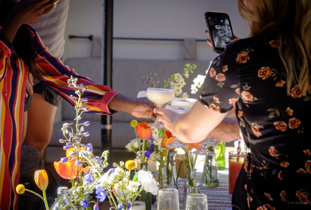 a woman taking a picture of a woman holding a glass of liquid