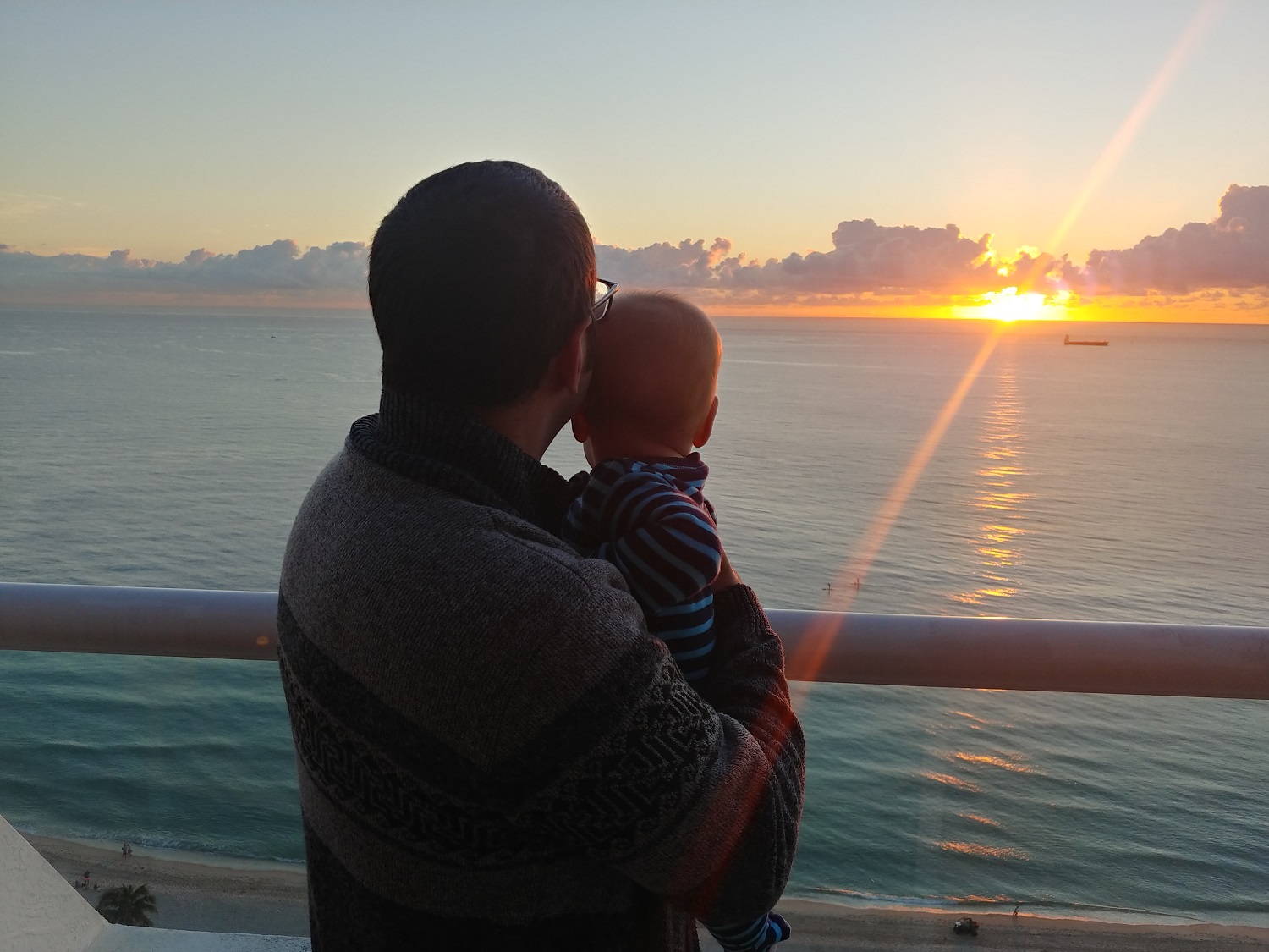 a man holding a baby by a railing overlooking the ocean