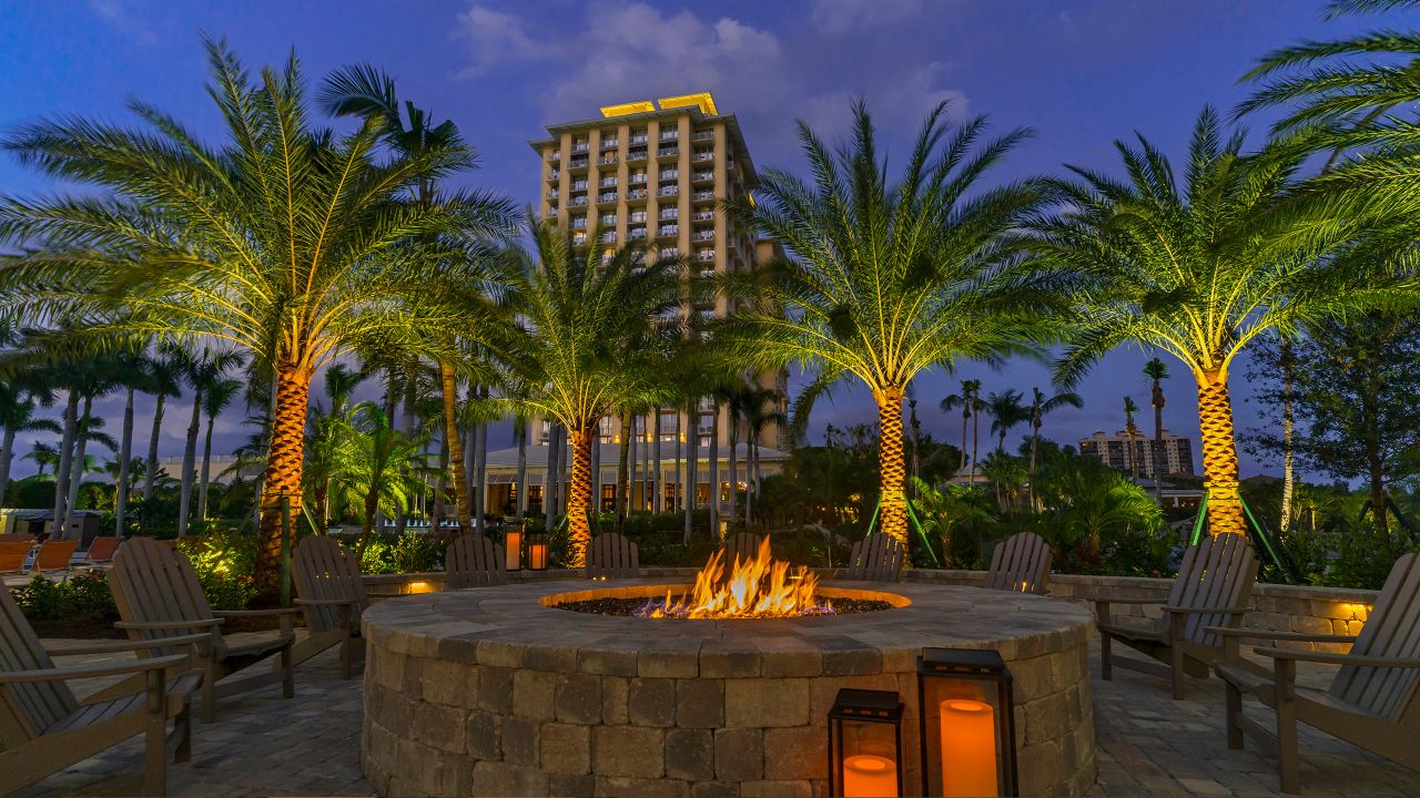a fire pit with palm trees and chairs in front of a building