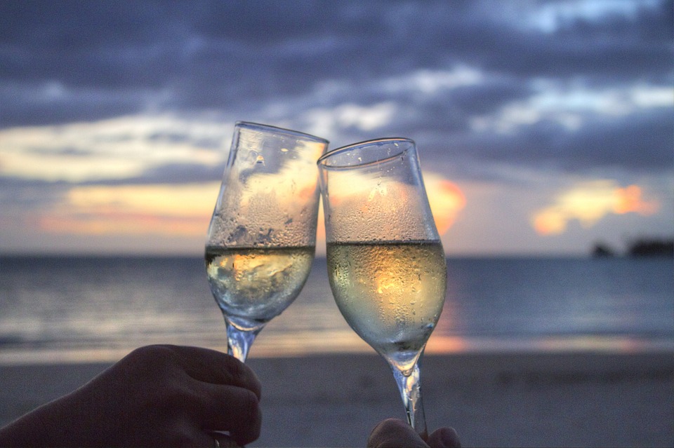 two hands holding wine glasses with a sunset in the background