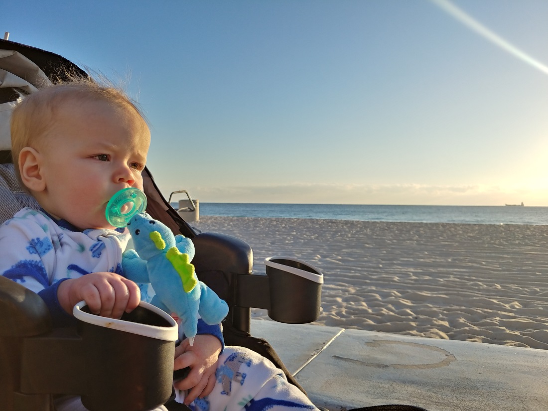 a baby sitting in a stroller on a beach