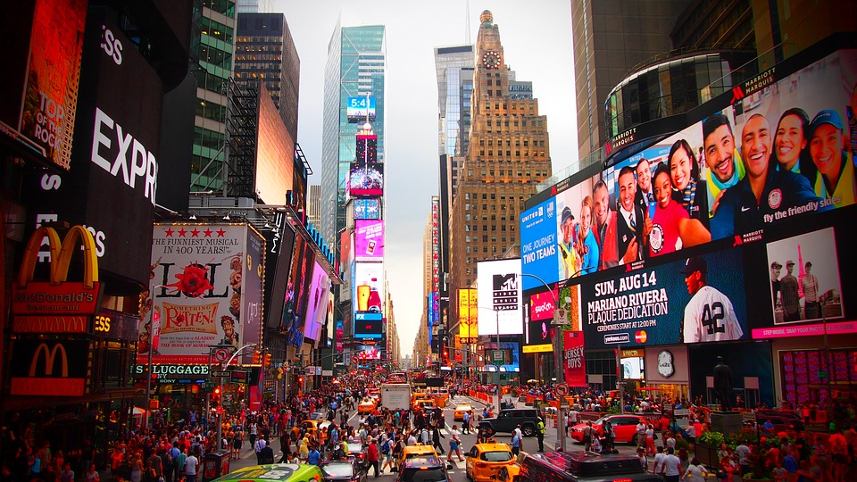 a busy city street with many people and billboards with Times Square in the background