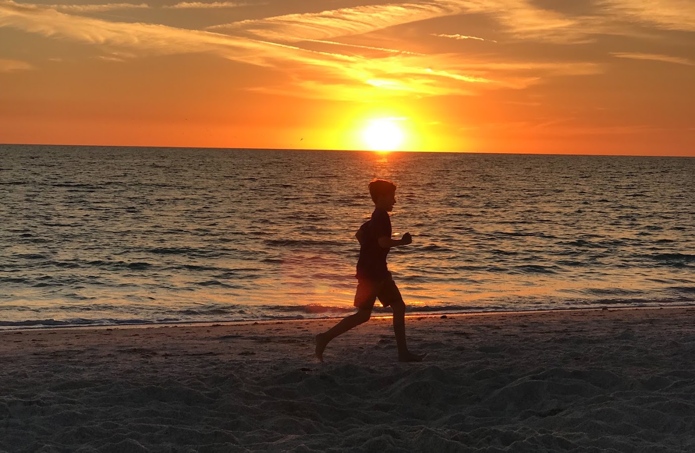 a boy running on a beach at sunset