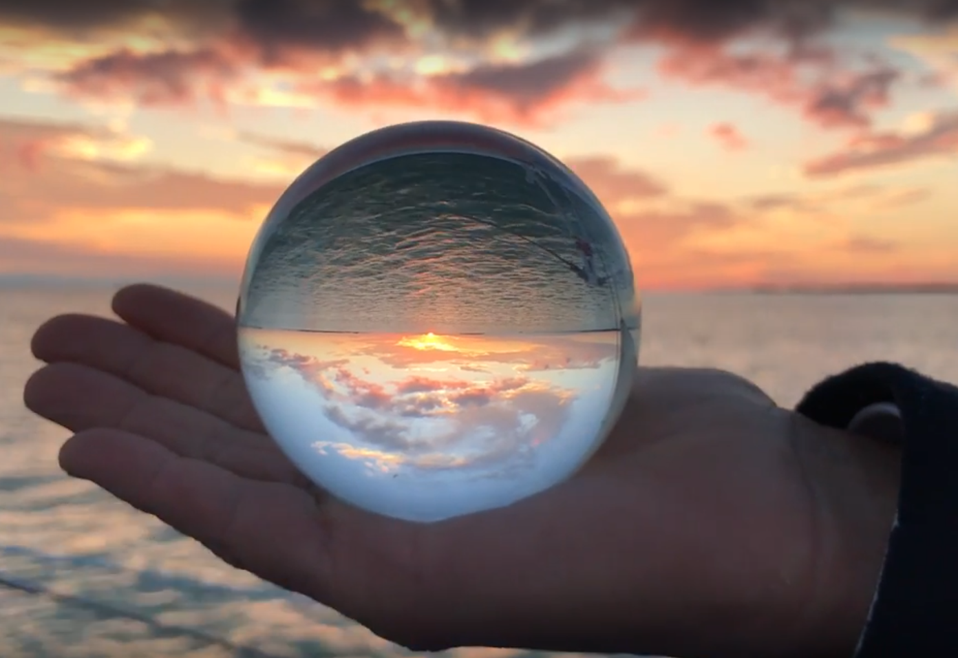 a hand holding a crystal ball with a sunset in the background