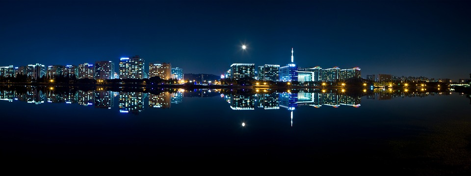 a city skyline at night with the moon reflecting on water