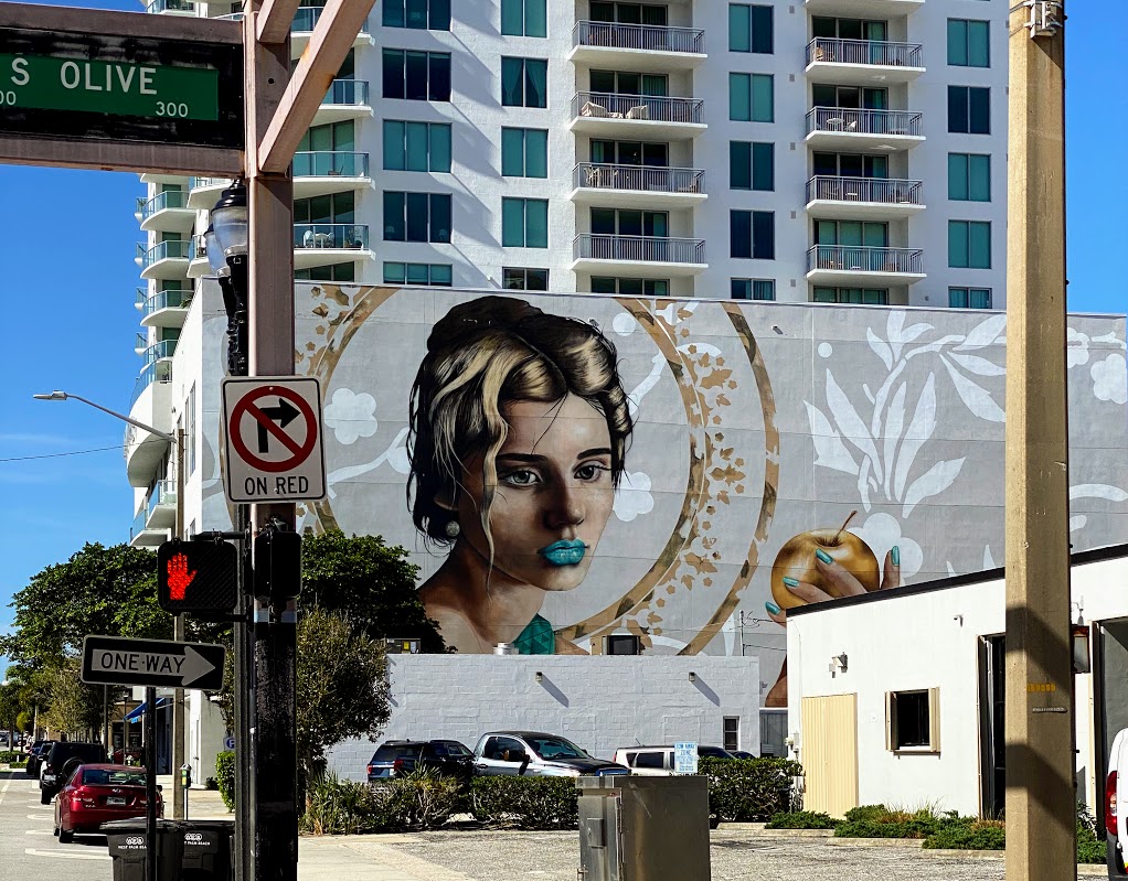 a street sign with a painting of a woman on the side of a building