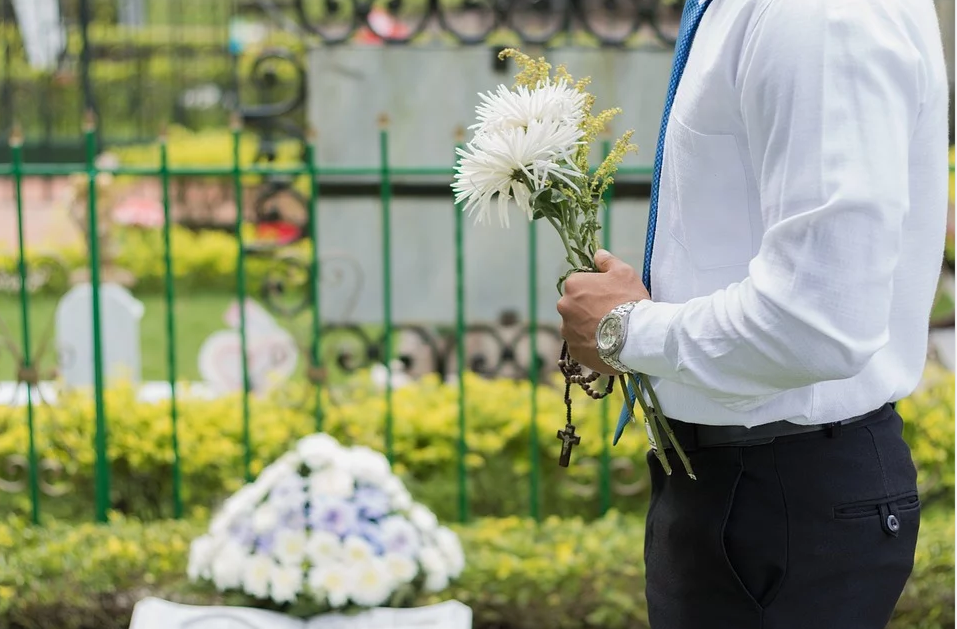 a man holding flowers in front of a grave