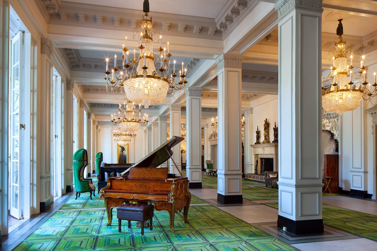 a piano in a room with green carpet and chandeliers