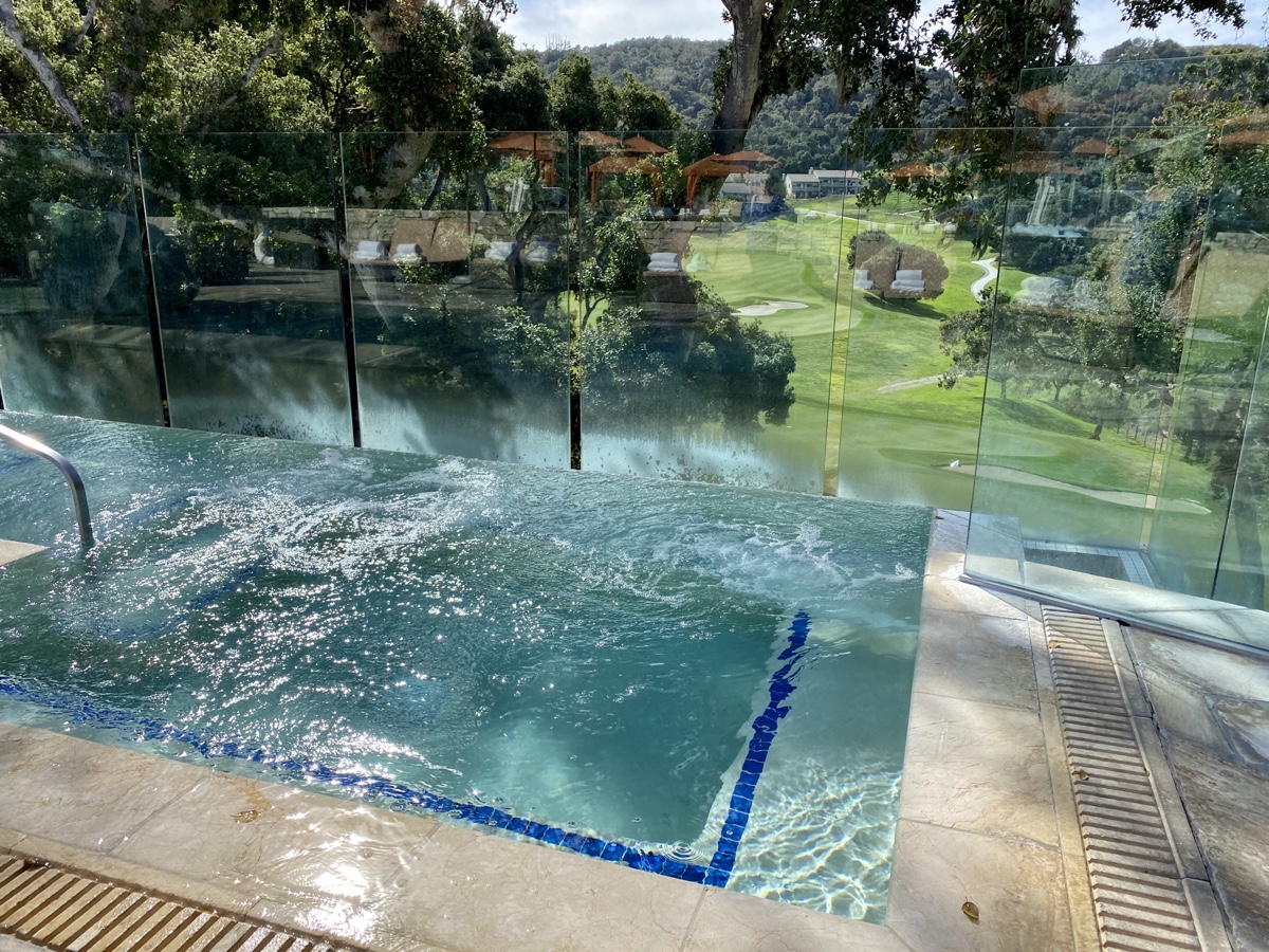 a pool with a glass fence and a golf course in the background