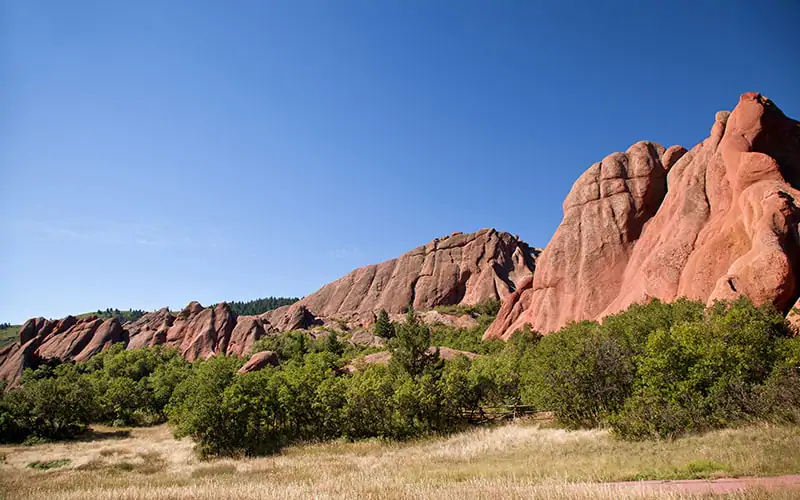 a large red rock formation with trees and blue sky with Capitol Reef National Park in the background