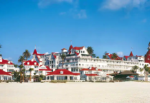 a large white building with red roofs on a beach with Hotel del Coronado in the background