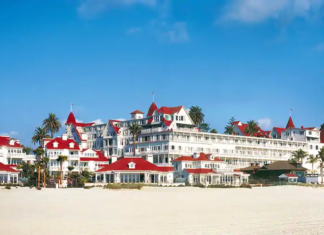a large white building with red roofs on a beach with Hotel del Coronado in the background
