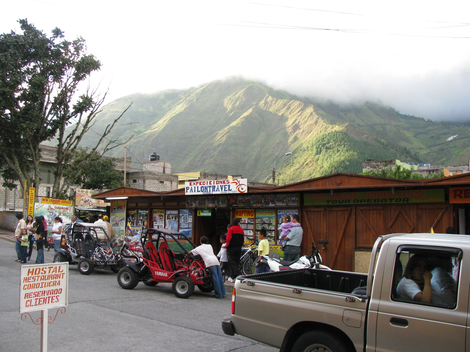 a group of people outside a building with vehicles parked in front of a mountain