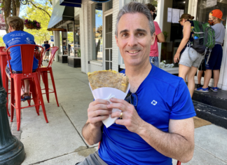 a man sitting on a sidewalk eating a sandwich