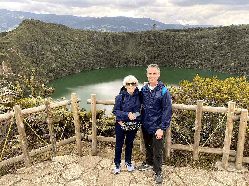a man and woman standing on a ledge with a lake in the background