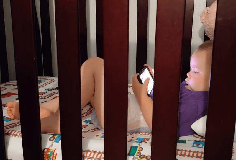 a baby lying in a crib holding a phone