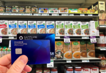 a hand holding a credit card in front of a shelf of food