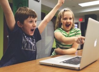 a boy and girl with their hands up in front of a laptop