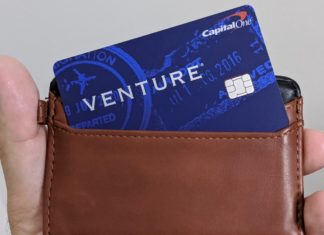 a hand holding a brown wallet with a blue credit card inside