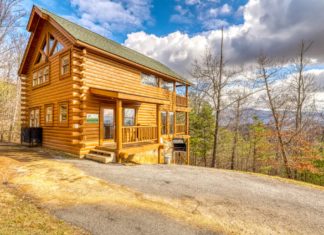 a log cabin with a driveway and trees in the background