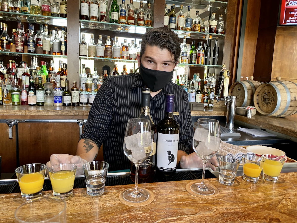 a man wearing a face mask behind a bar with glasses and bottles
