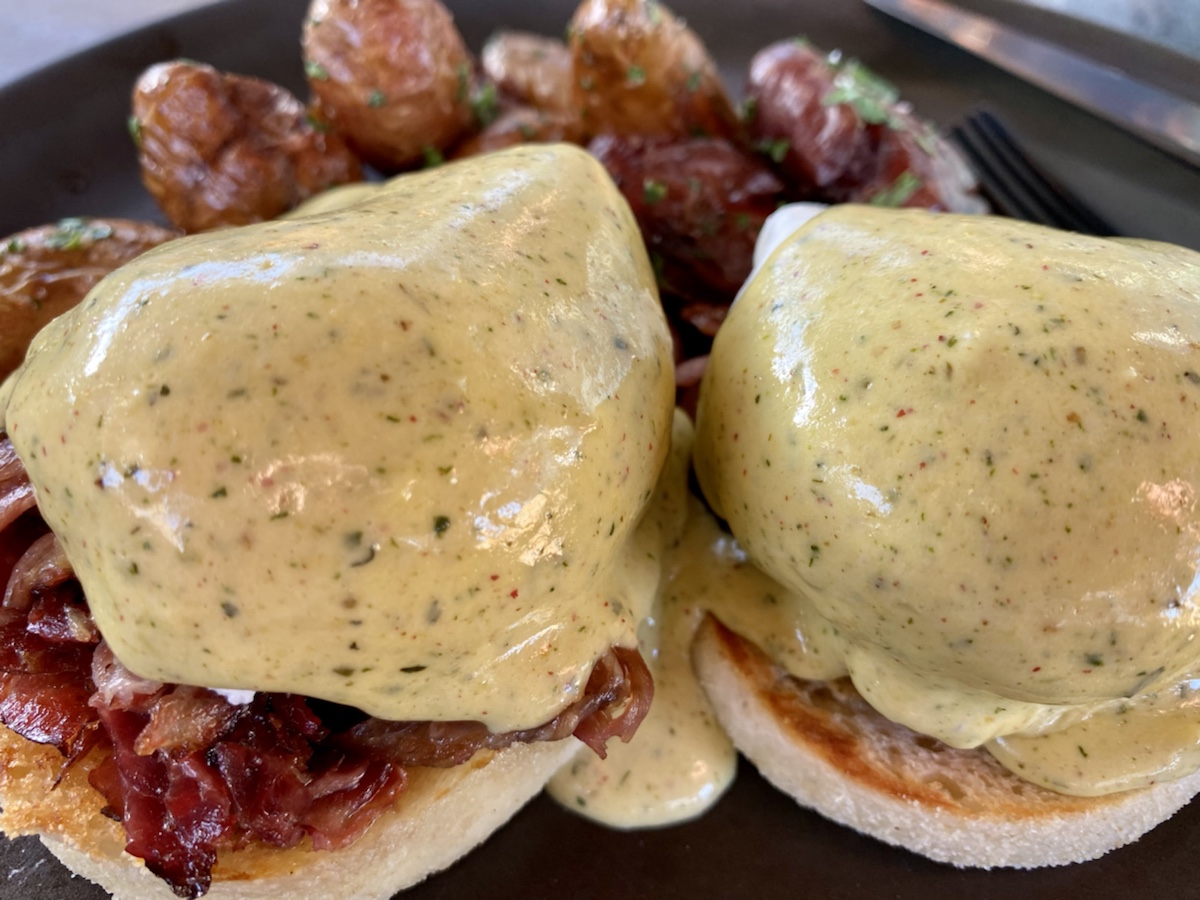 a plate of eggs benedict with meat and potatoes