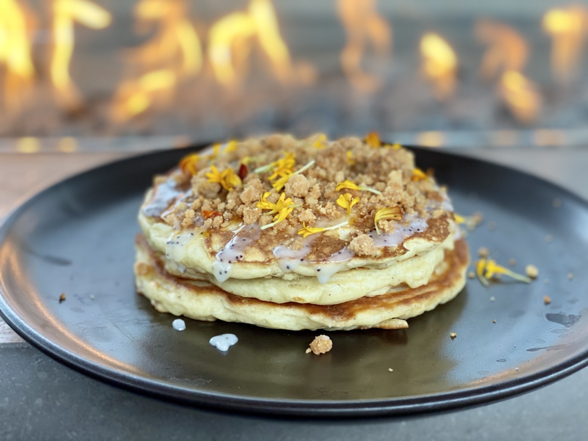 a stack of pancakes with crumbles and toppings on a black plate
