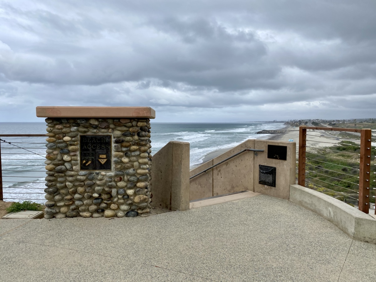 a stone wall with a railing overlooking a beach