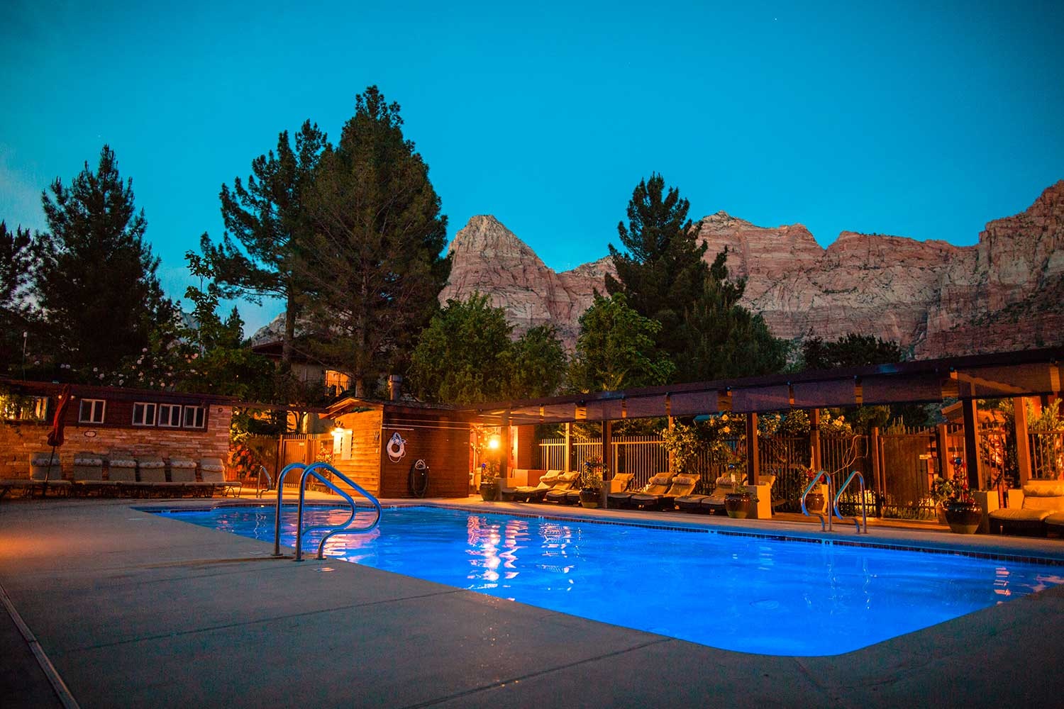 a pool with a covered deck and a building with mountains in the background