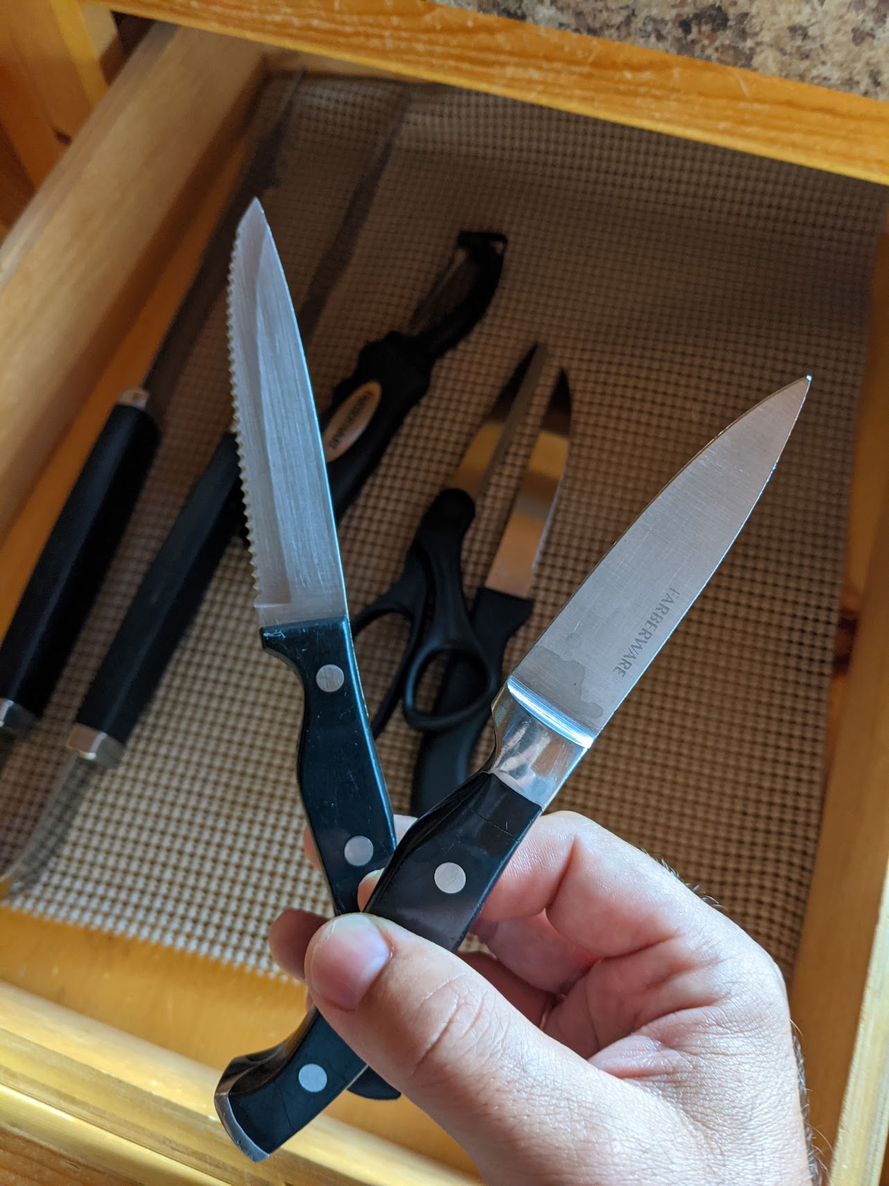 a hand holding a knife and a knife in a drawer