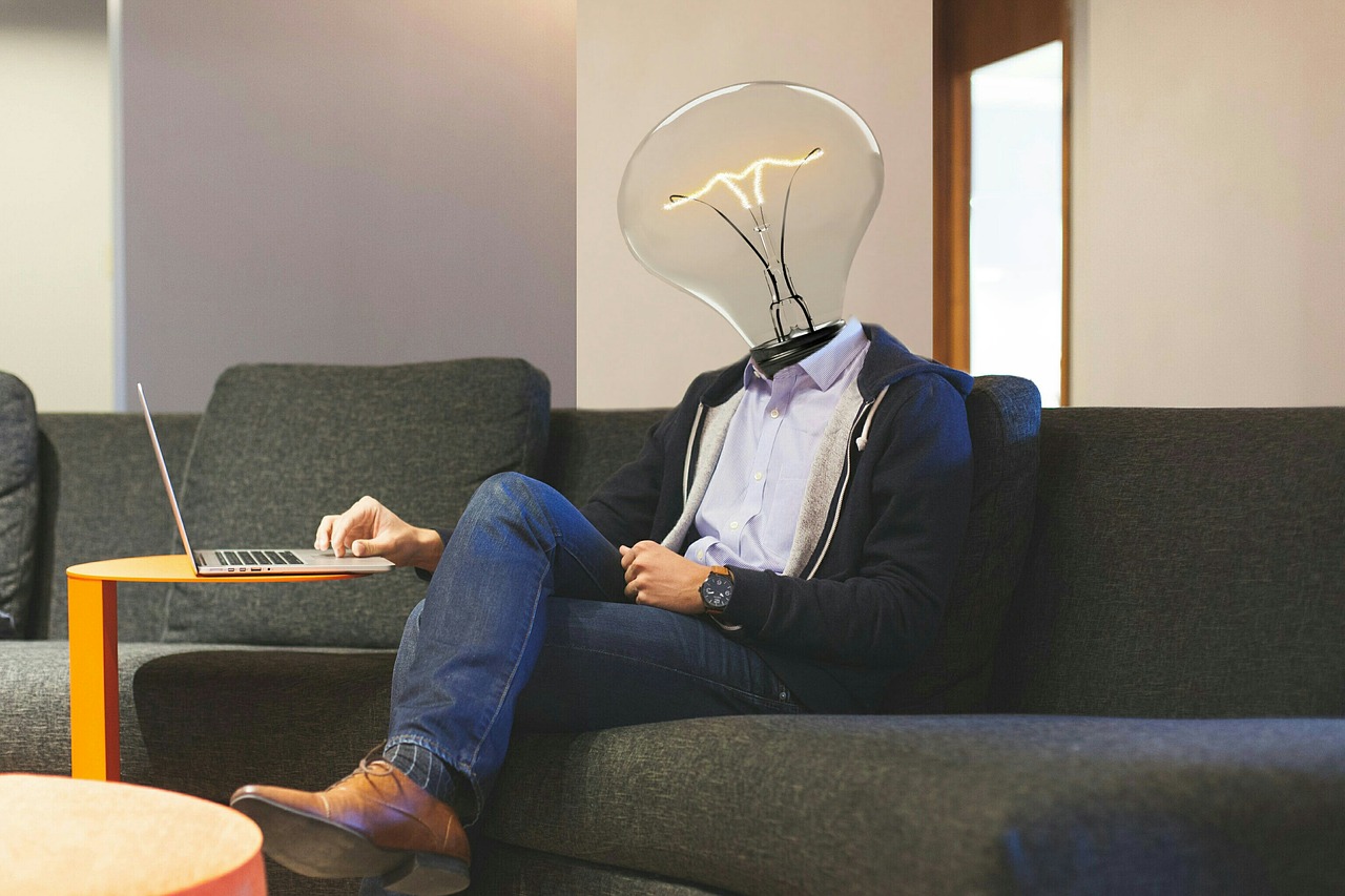 a person sitting on a couch with a laptop and a light bulb head