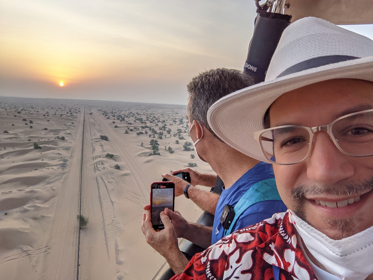a selfie of a man in a hat and glasses with a desert landscape