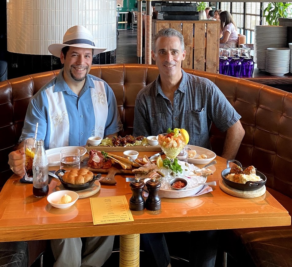 two men sitting at a table with food on it