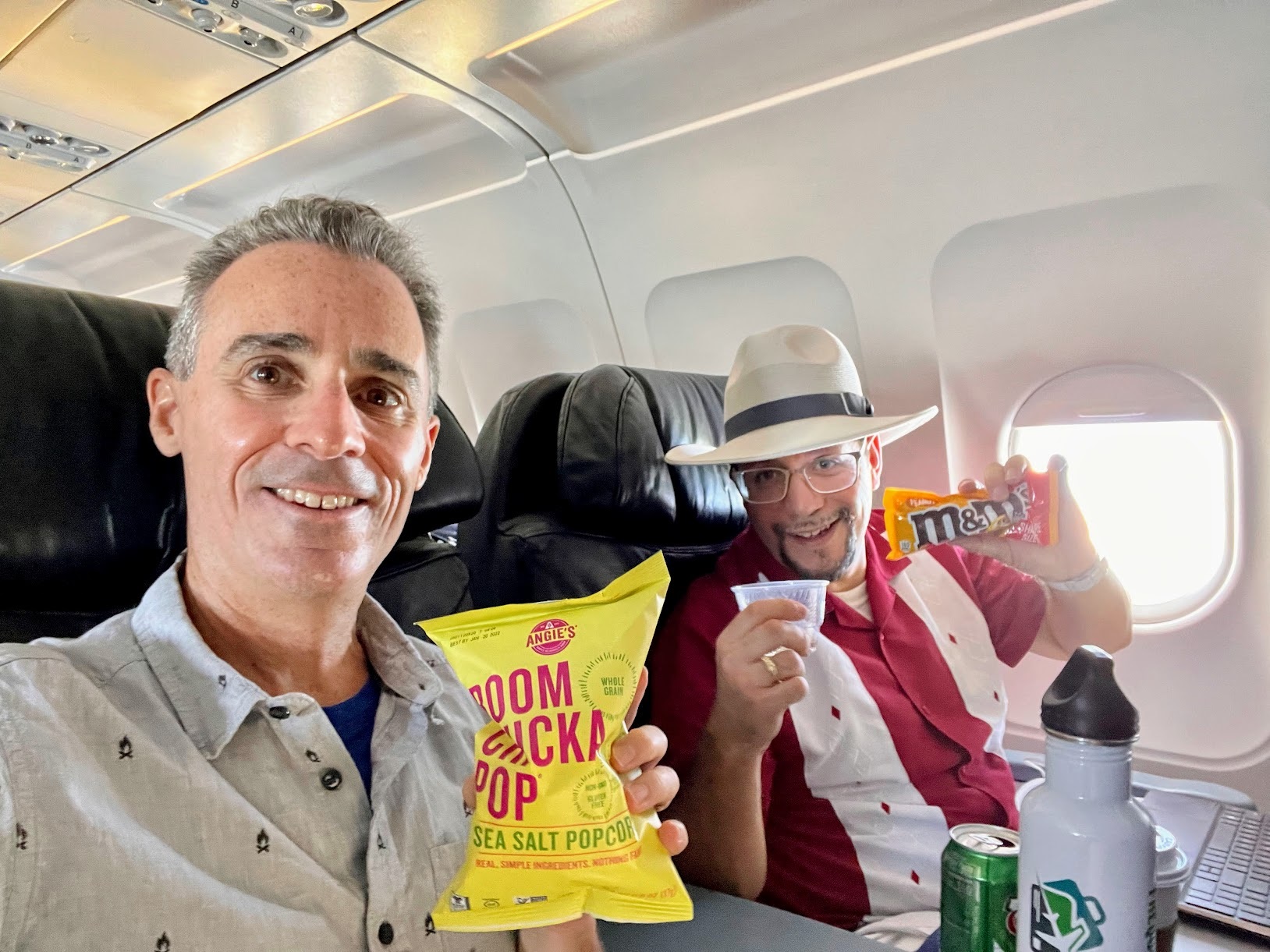 two men sitting in a plane eating snacks