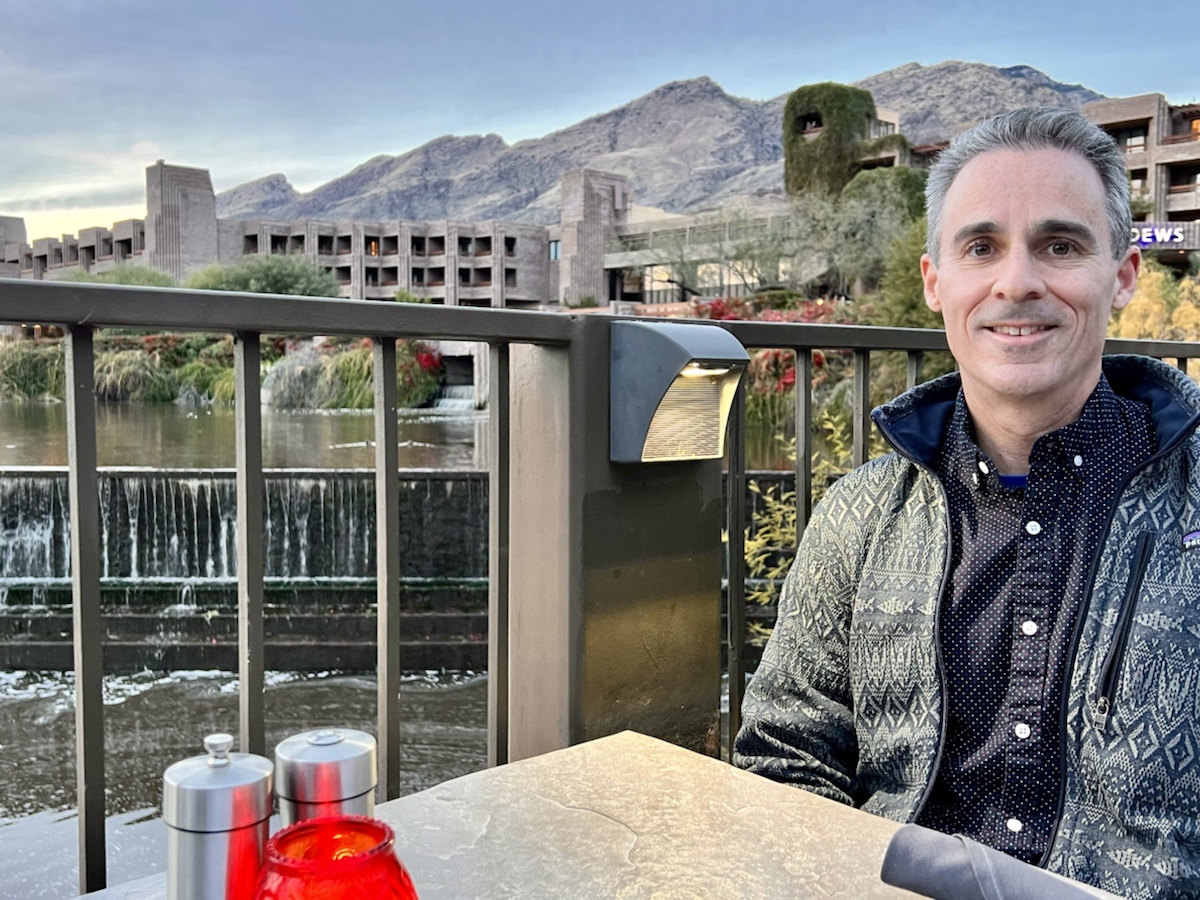 a man sitting at a table with a waterfall and mountains in the background