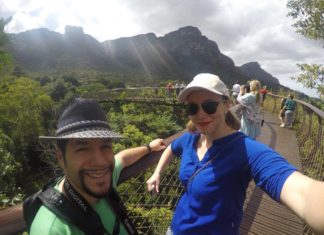 a man and woman taking a selfie on a bridge over a forest