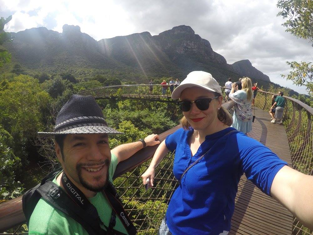 a man and woman taking a selfie on a bridge over a forest